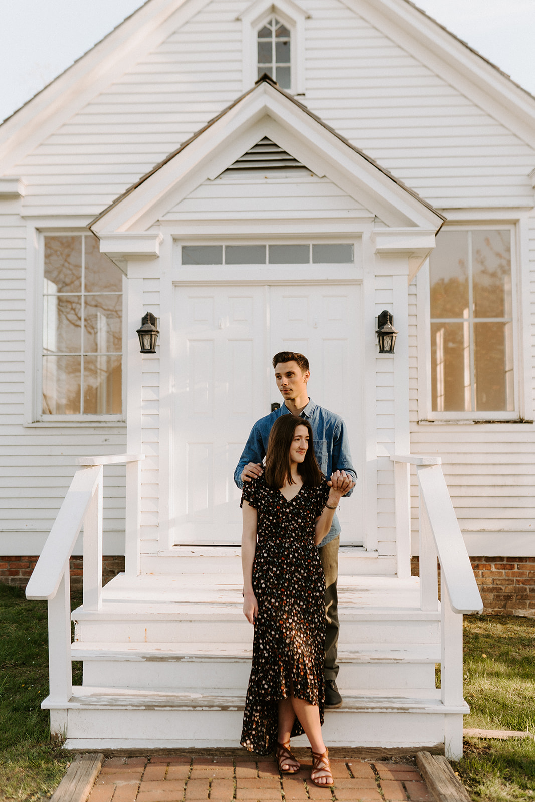 couple hugging in front of white church during engagement session